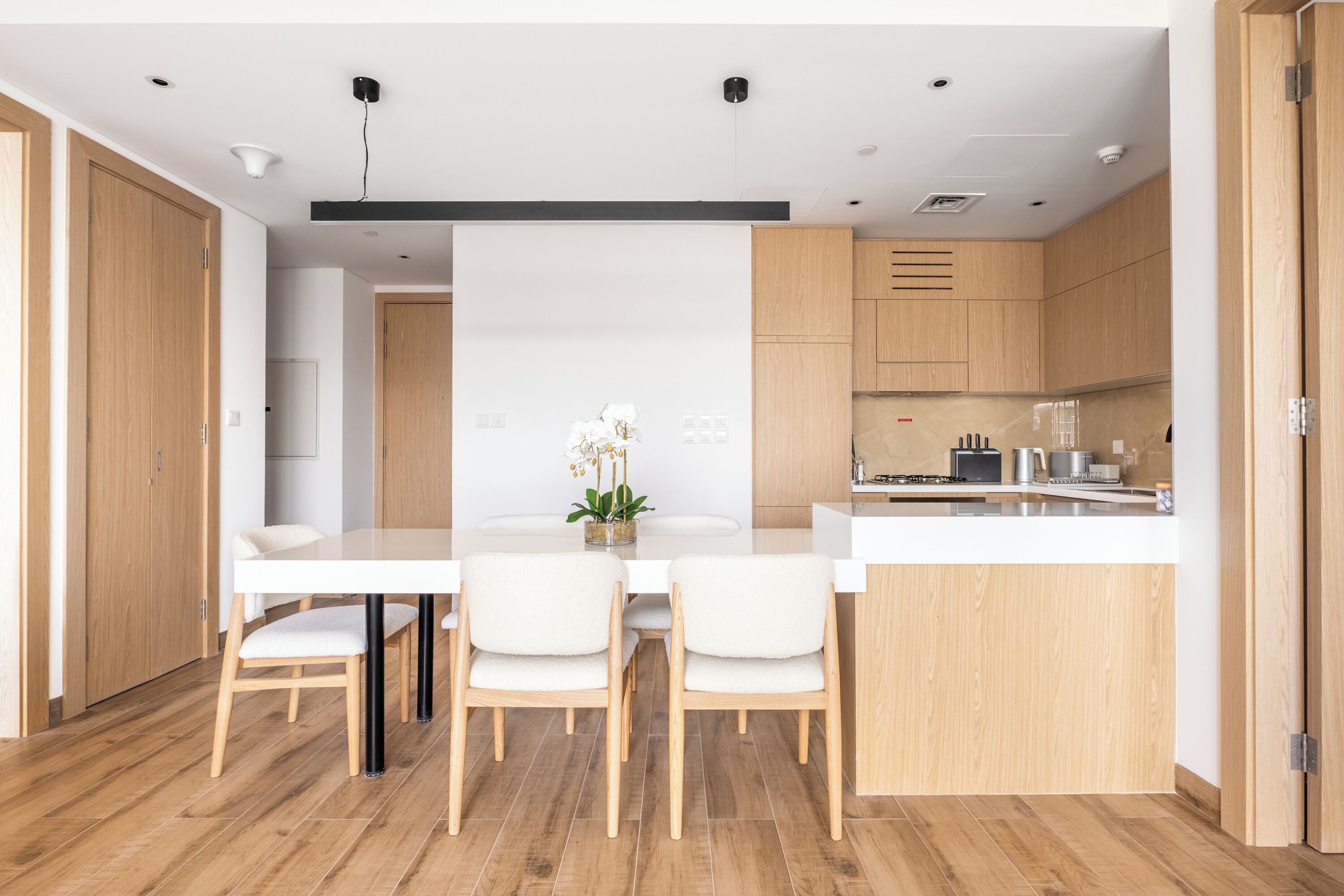 Une cuisine moderne avec des meubles en bois, un plan de travail blanc et un coin repas comprenant une table et des chaises blanches.