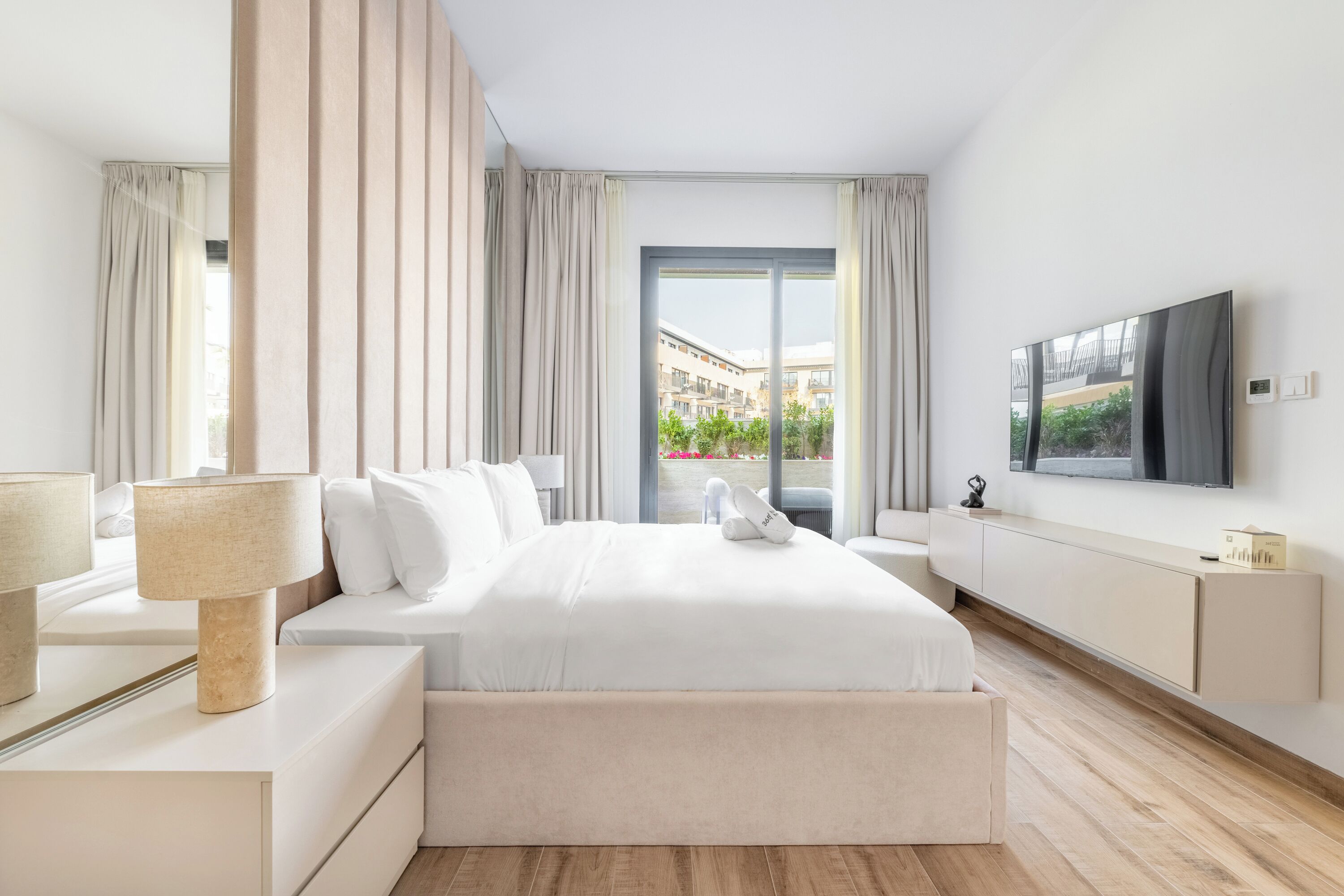 Een moderne hotelkamer met een groot bed, een aan de muur bevestigde televisie en uitzicht op de stad door het raam.