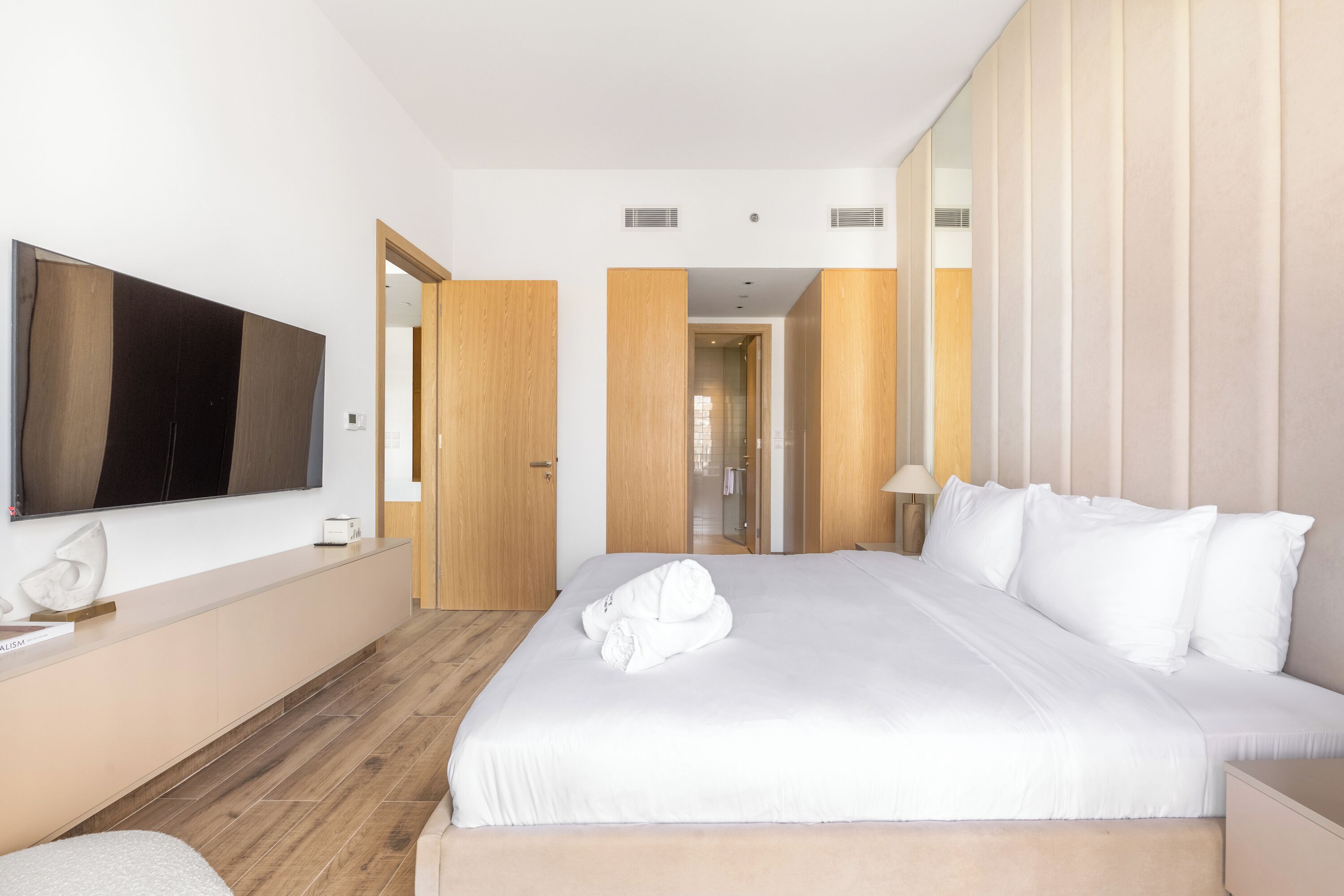 A modern hotel room with a large bed, a flat-screen TV, a wooden floor, and a large mirror.