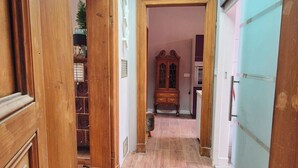A hallway with wooden flooring, a ceiling light, a wooden cabinet, and a door leading to another room.