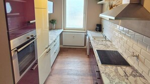 A compact kitchen with a built-in oven, a microwave, and a sink. There is a window above the sink, and a ceiling light fixture.