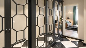 A hallway with a geometric-patterned door, a checkered floor, and a glimpse of a living area with a sofa and lamp. - Apartments Florence - Granduca Penthouse with stunning terrace (Florence)