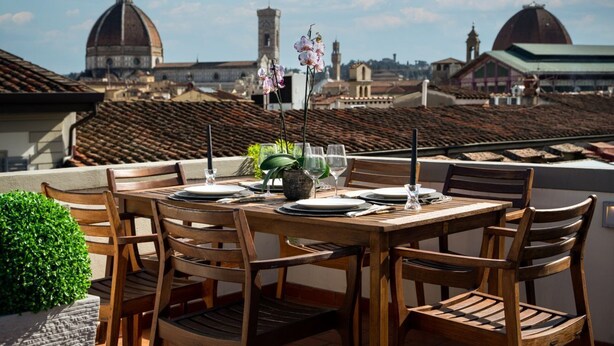 A dining table set outdoors with chairs, a potted plant, and wine glasses. - Apartments Florence - Granduca Penthouse with stunning terrace (Florence)