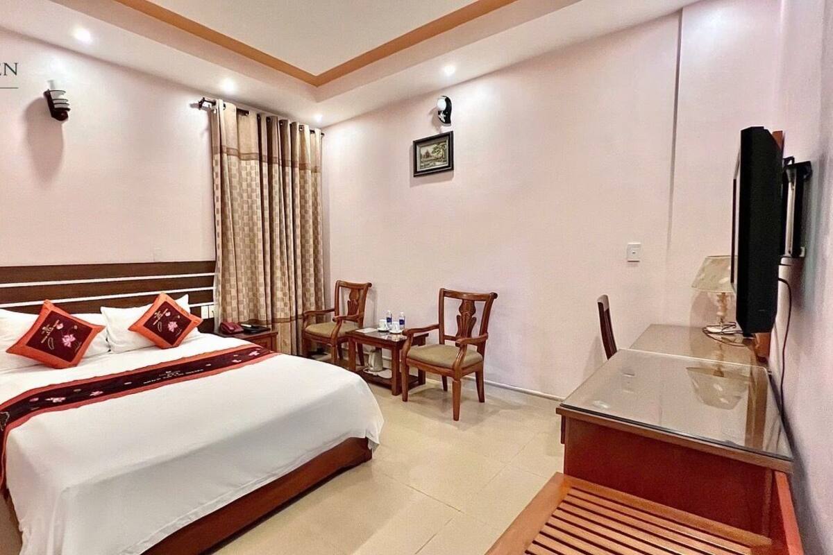 A hotel room with a bed, a desk, a chair, a television, and a window with curtains.