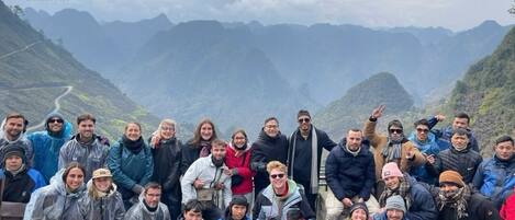 Un groupe de personnes se trouve dans une région montagneuse, le long d’une route sinueuse.