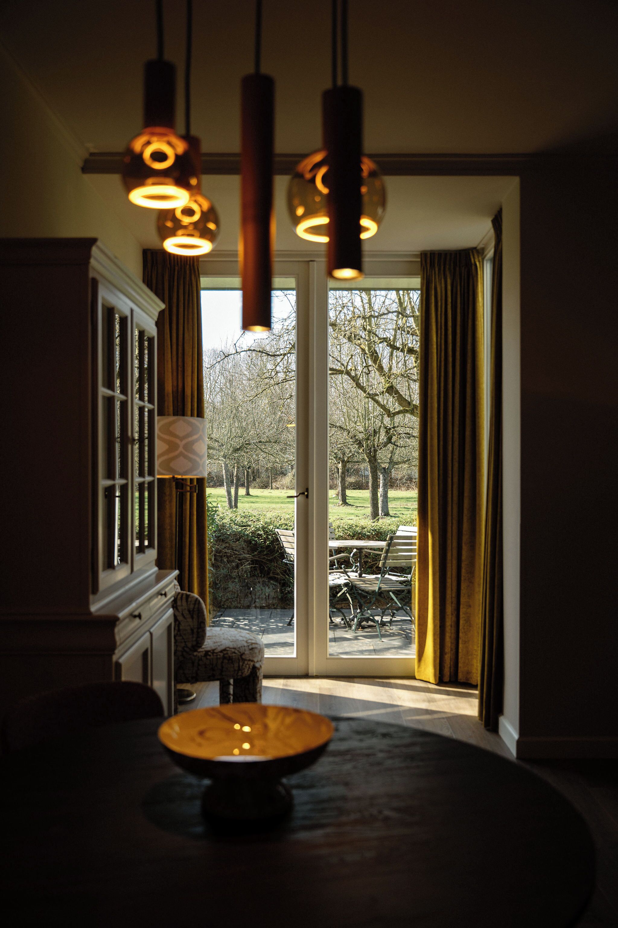 A dining area with a table and chairs, a window with curtains, and hanging pendant lights.