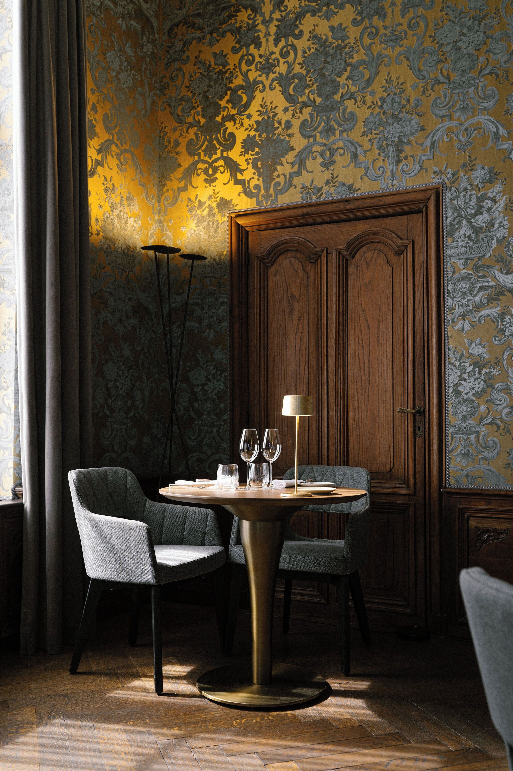 A dining area with a round table, two chairs, a lamp, and a wooden cabinet.