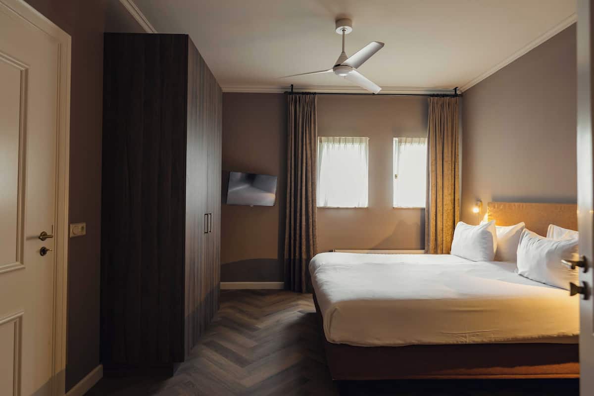 Een hotelkamer met een bed, een plafondventilator, een televisie en een raam met gordijnen.