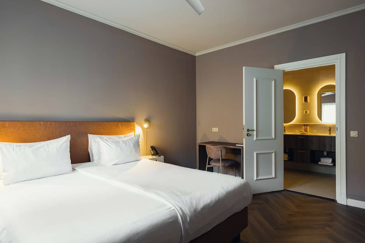 Een hotelkamer met een bed, nachtkastje, lamp en een open deur naar een badkamer.