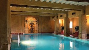 An indoor swimming pool with a tiled floor, a statue, and potted plants.