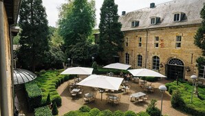 A courtyard with outdoor seating, surrounded by trees and a historic building.