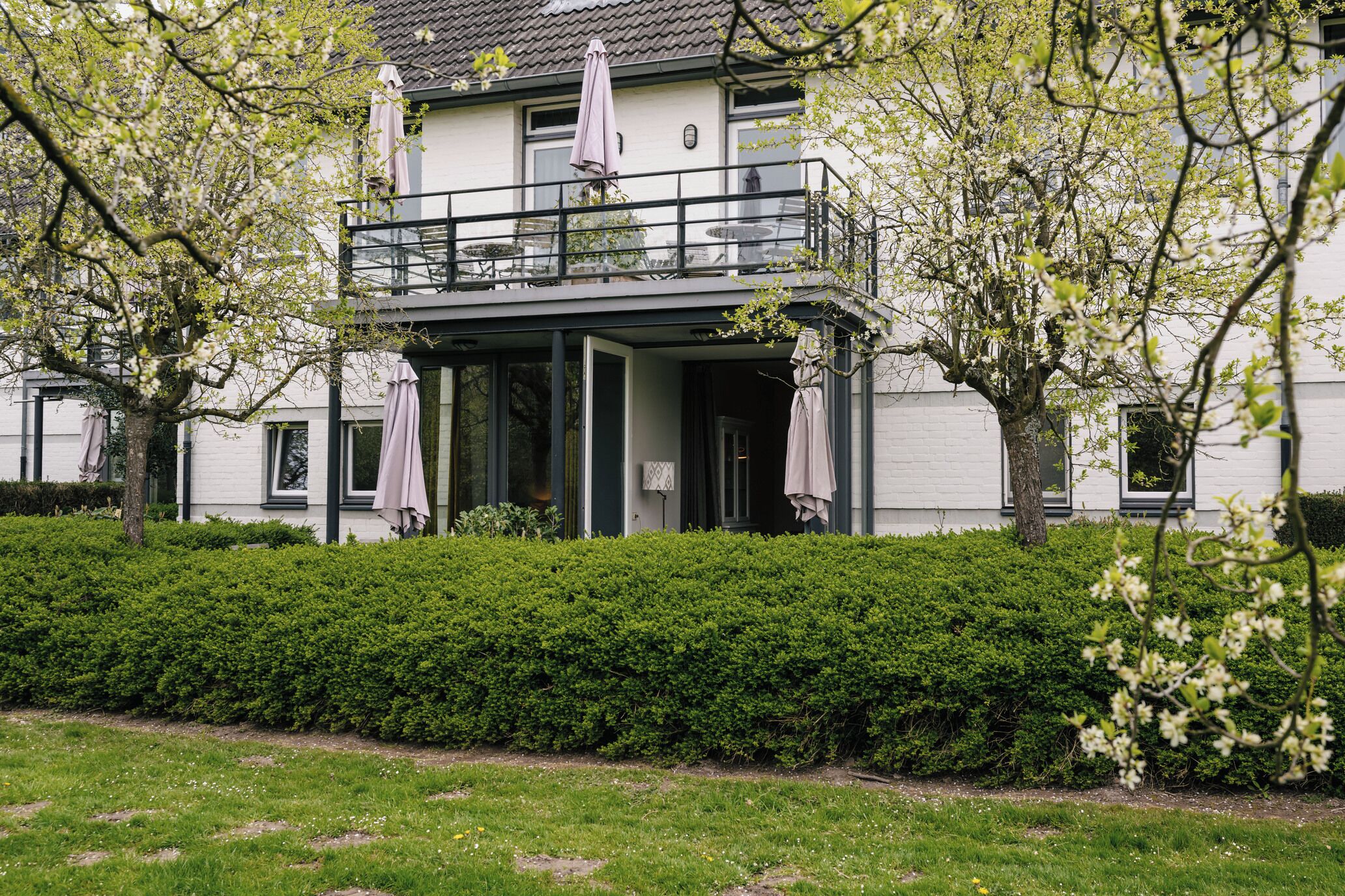 A two-story house with a balcony, a covered entrance, and a well-maintained garden.