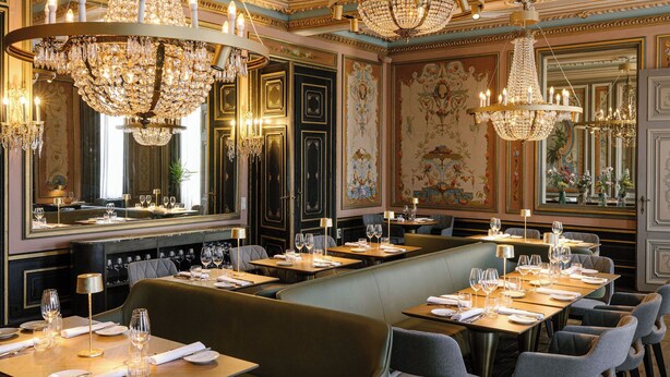 A restaurant with multiple dining tables, elegant chandeliers, and ornate wall decorations.