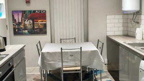 Eine kleine Küche mit Esstisch, Stühlen, einem gemusterten Teppich, einem weißen Heizkörper und einem Bild an der Wand.