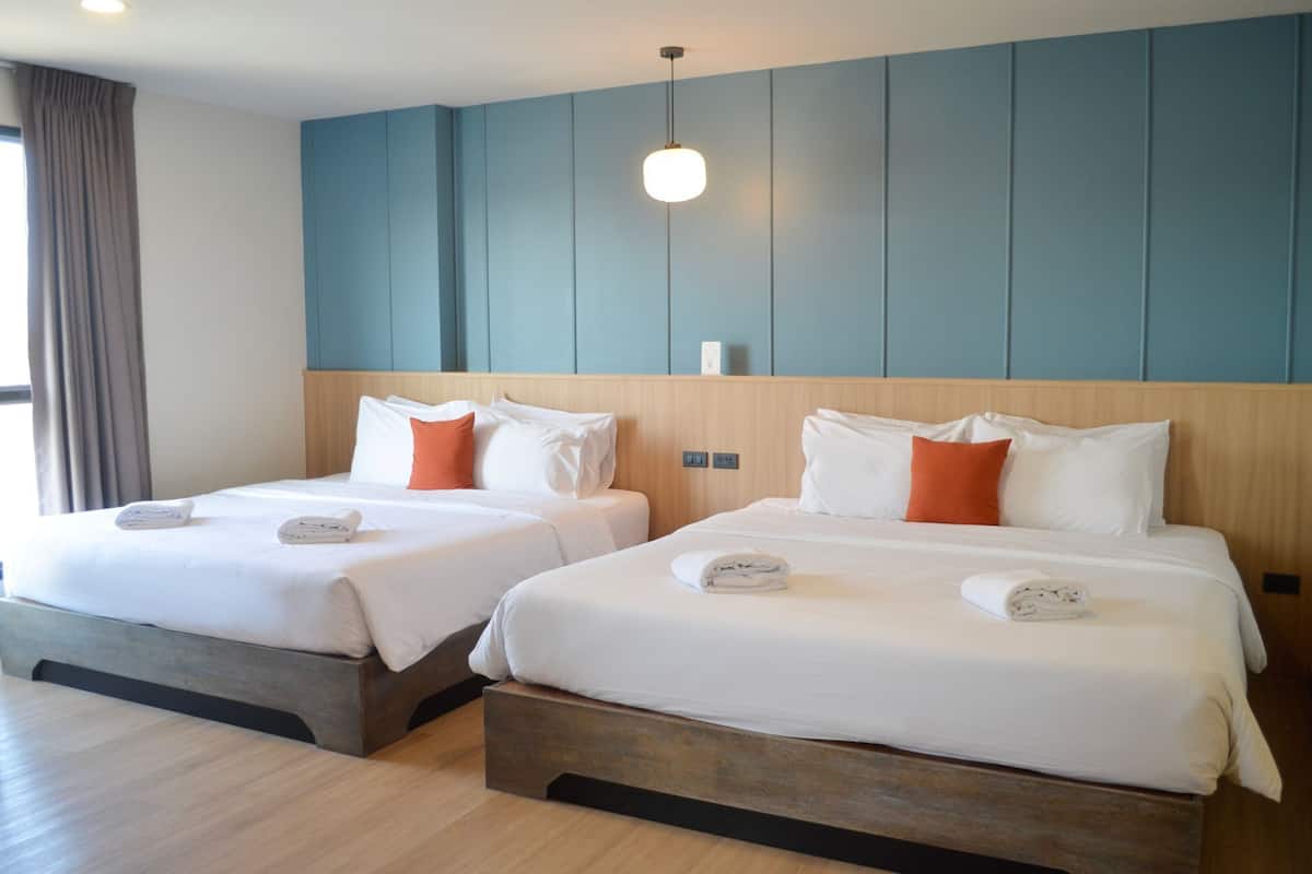 Une chambre d’hôtel avec deux lits, chacun doté de draps blancs et d’oreillers orange, d’une tête de lit en bois et d’un mur d’accent bleu.
