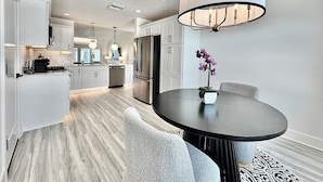 Una cocina moderna con armarios blancos, un refrigerador de acero inoxidable y un comedor con una mesa redonda y sillas.