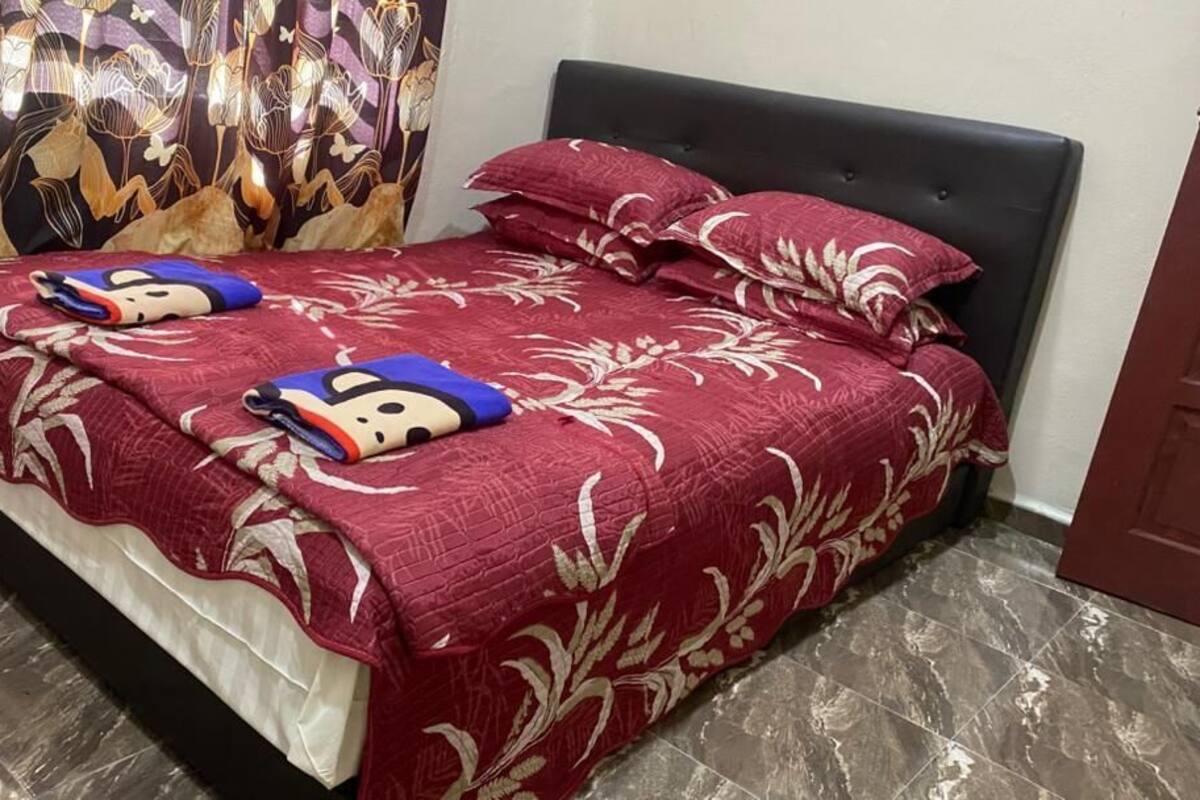 A bed with a red floral bedspread and two pillows, a dark headboard, and a patterned curtain.