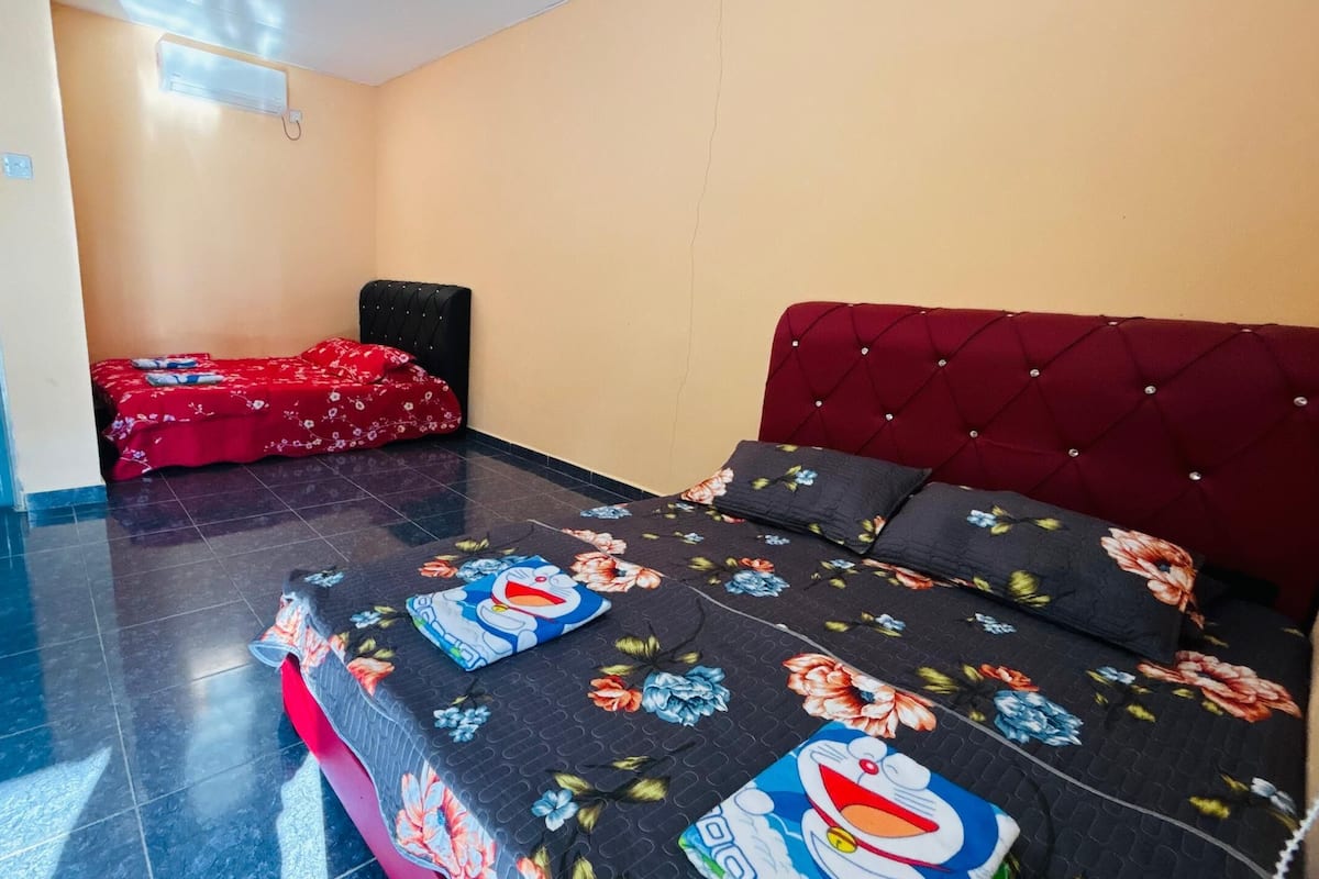 A hotel room with a bed, a red upholstered headboard, a red bedspread, and a floral-patterned pillow.