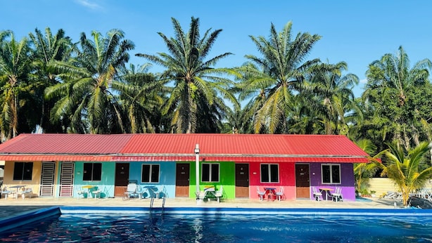 A colorful building with a red roof and multiple rooms, each with a different color. In front of the building, there is a swimming pool with lounge chairs and umbrellas.
