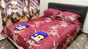 A bed with a red floral bedspread and two Mickey Mouse plush toys on it.