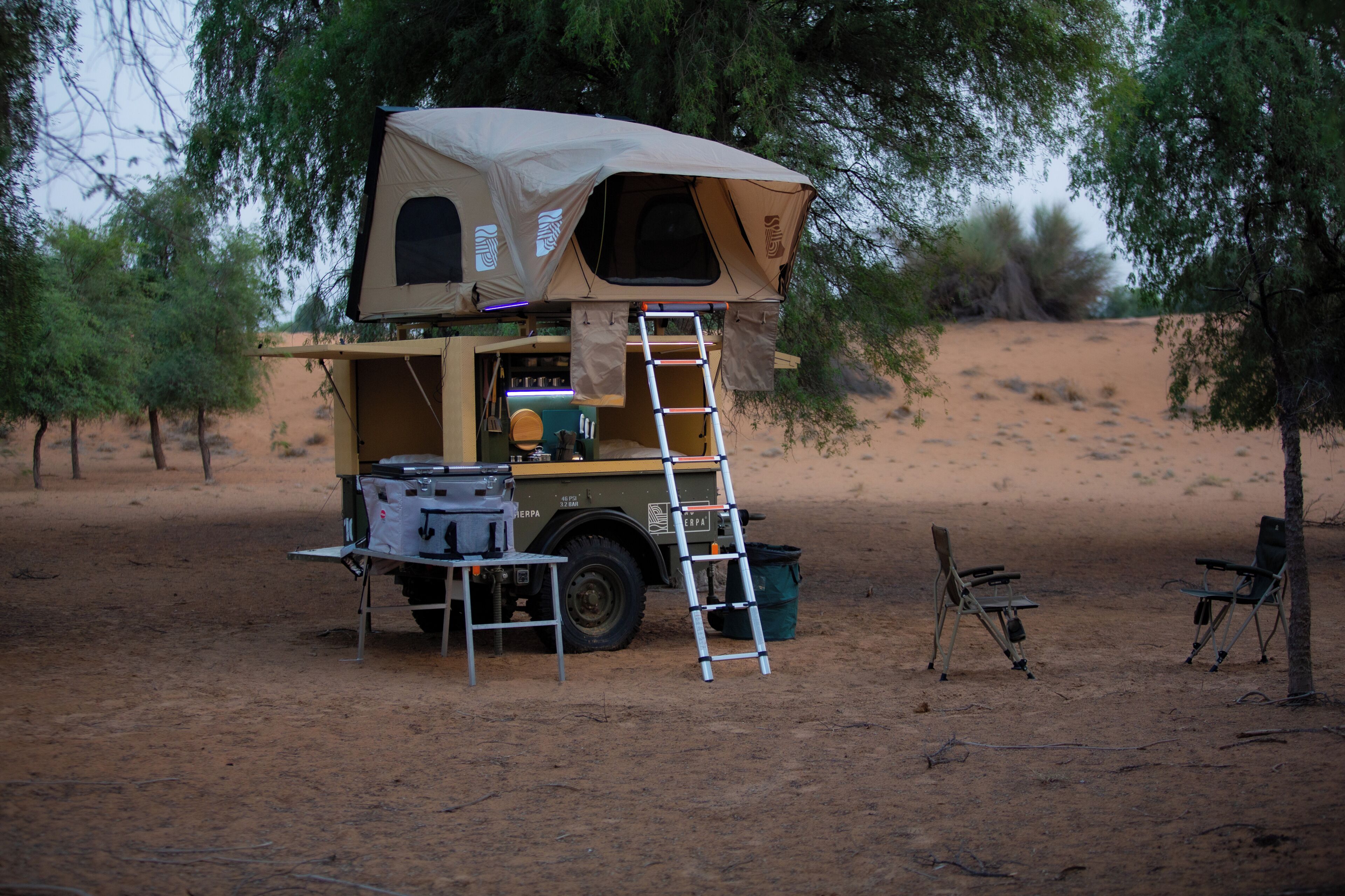 Un vehículo con techo tipo tienda de campaña, escalera y equipo de camping.