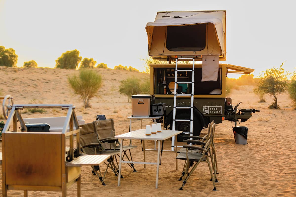 A safari vehicle with a tent, a table, chairs, and a ladder.