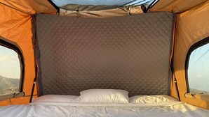 Una tienda con pared interior acolchada, una cama con ropa blanca y dos ventanas.
