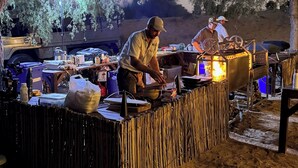 Un camping con una mesa de madera, equipo de cocina y una tienda de campaña al fondo.