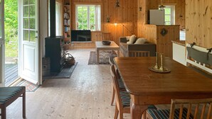 A cozy cabin interior with a wooden dining table, a sofa, a television, and a bookshelf. - Cozy home in Sjællands Odde with WiFi (Sjællands Odde)