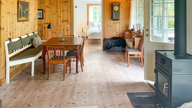 A cozy wooden cabin interior with a dining table, bench, and chairs, a bed, a fireplace, and a large window. - Cozy home in Sjællands Odde with WiFi (Sjællands Odde)