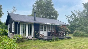 A small, single-story house with a dark roof and white trim, featuring a porch with wooden chairs and a table. - Cozy home in Sjællands Odde with WiFi (Sjællands Odde)