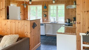 A cozy cabin-style kitchen with wooden walls, a built-in dishwasher, and a dining area with a table and chairs. - Cozy home in Sjællands Odde with WiFi (Sjællands Odde)
