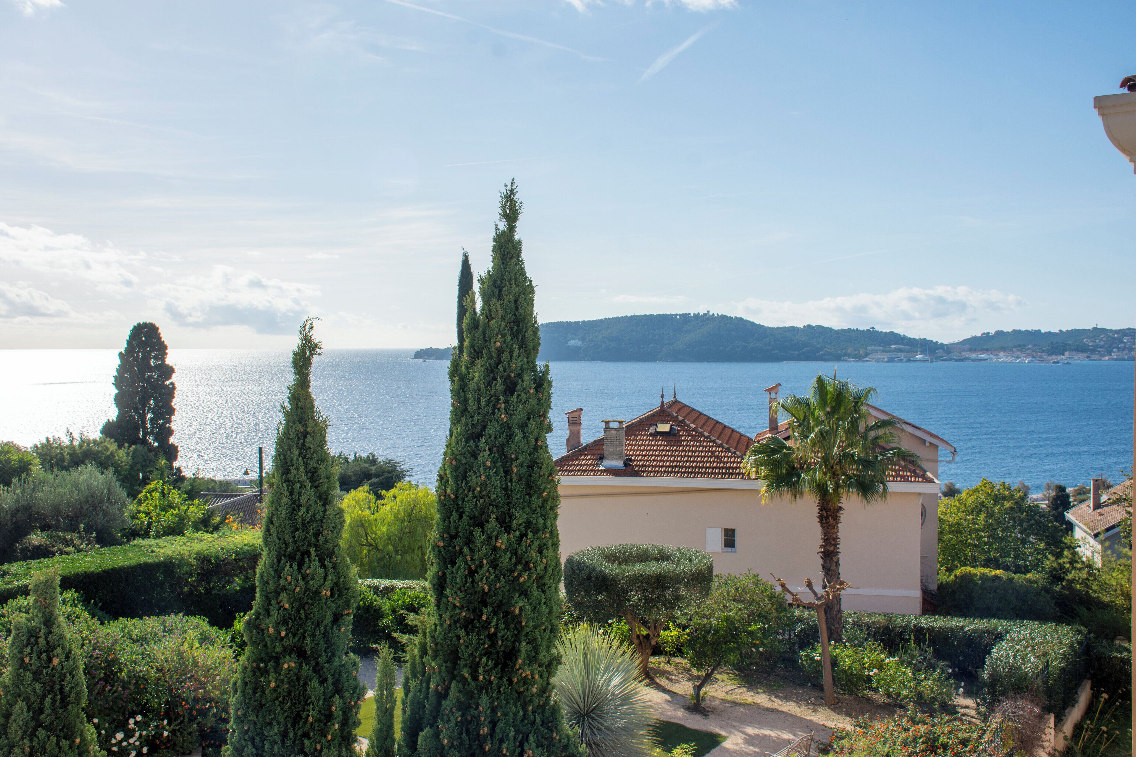 Une propriété située sur la côte, avec une maison de style méditerranéen, un jardin luxuriant et une vue sur la mer.
