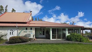 Un bâtiment à deux étages, avec un toit rouge, une véranda et une pelouse verdoyante.