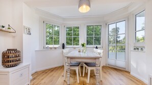 Un comedor con una mesa y sillas blancas, ventanas amplias y una lámpara colgante.