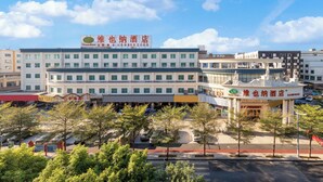 A hotel with a large sign, multiple floors, and a parking lot with trees. - Vienna Hotel International Airport  (Guangzhou)