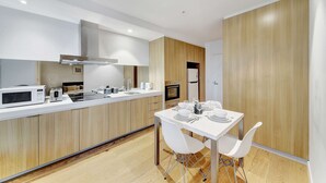Una cocina moderna con comedor, que cuenta con encimera blanca, armarios de madera y horno empotrado.