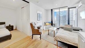 A modern bedroom with a bed, a chair, a TV, and a large window with a city view.