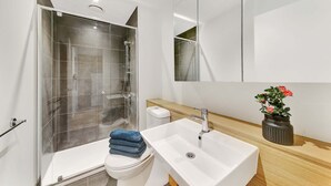 A modern bathroom with a glass shower enclosure, a white sink, and a wooden vanity.