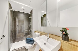 Une salle de bain moderne avec une douche à l’italienne en verre, un lavabo blanc et un meuble-lavabo en bois.