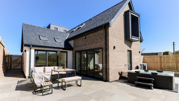 Ein modernes Haus mit Terrasse, Sitzgelegenheiten im Freien und Grillplatz.