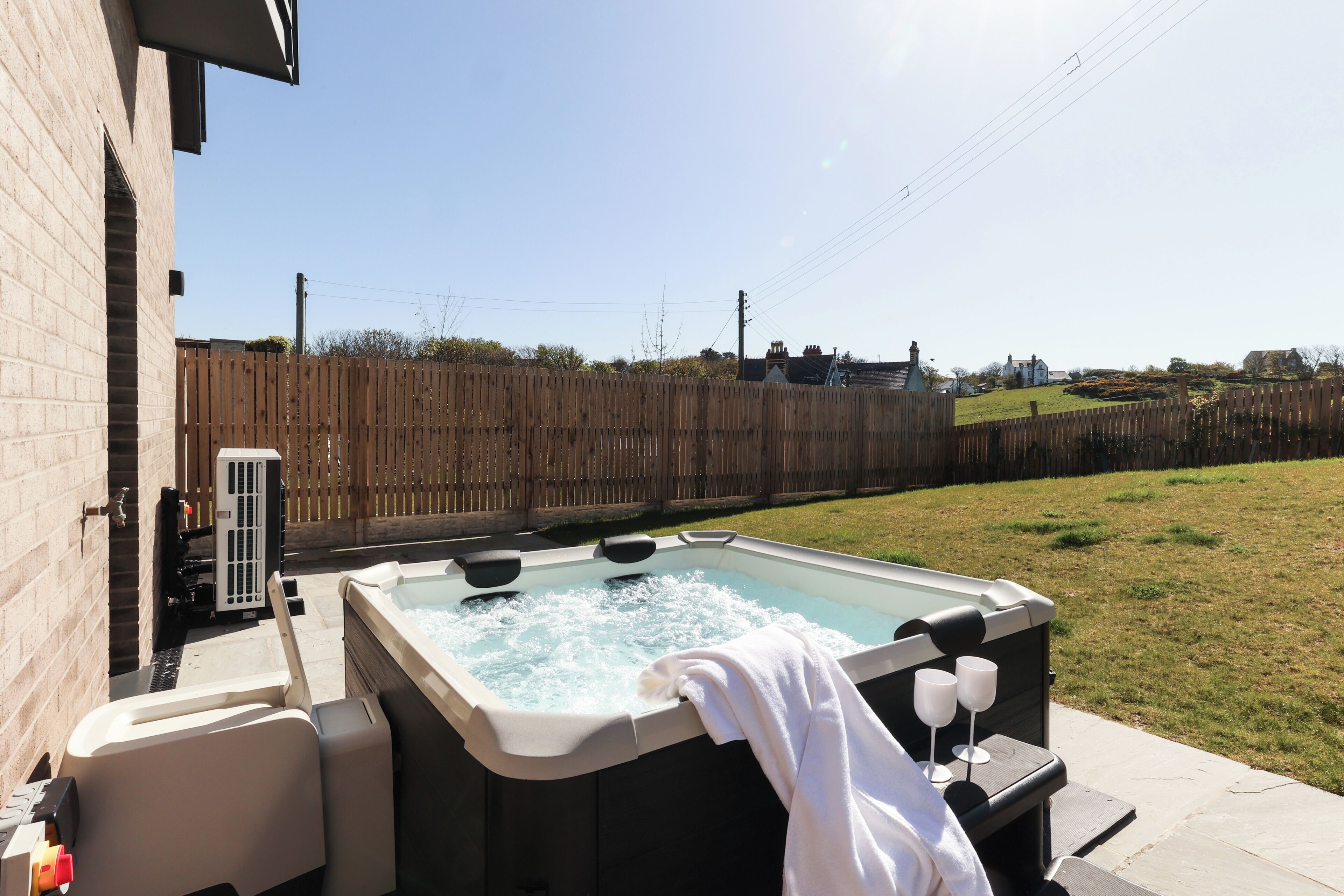 A hot tub with a towel and glasses, a brick wall, and a wooden fence in the background.