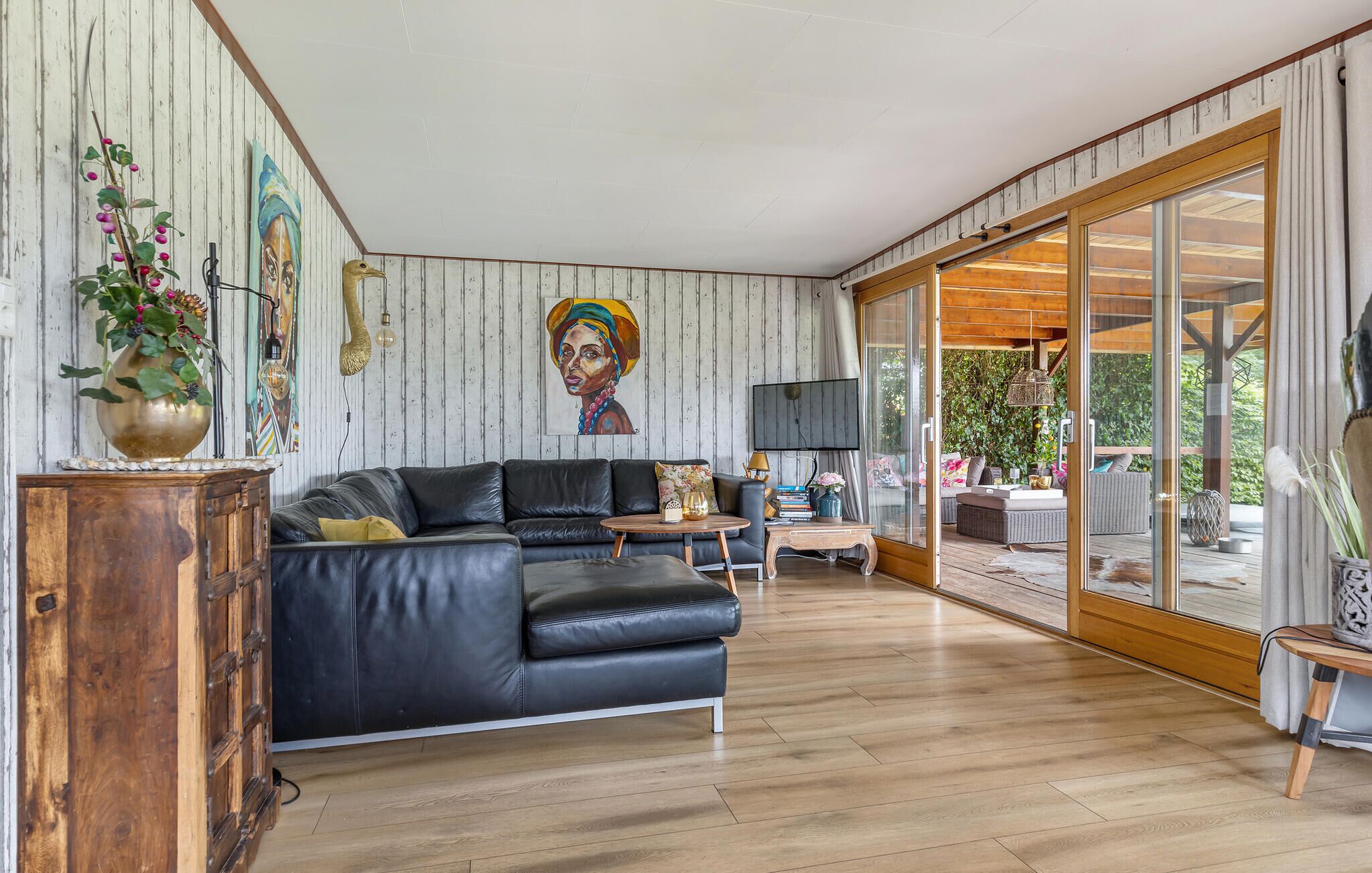 Amplia sala de estar con un sofá grande de cuero negro, piso de madera y puerta corrediza de vidrio que da a un área exterior.
