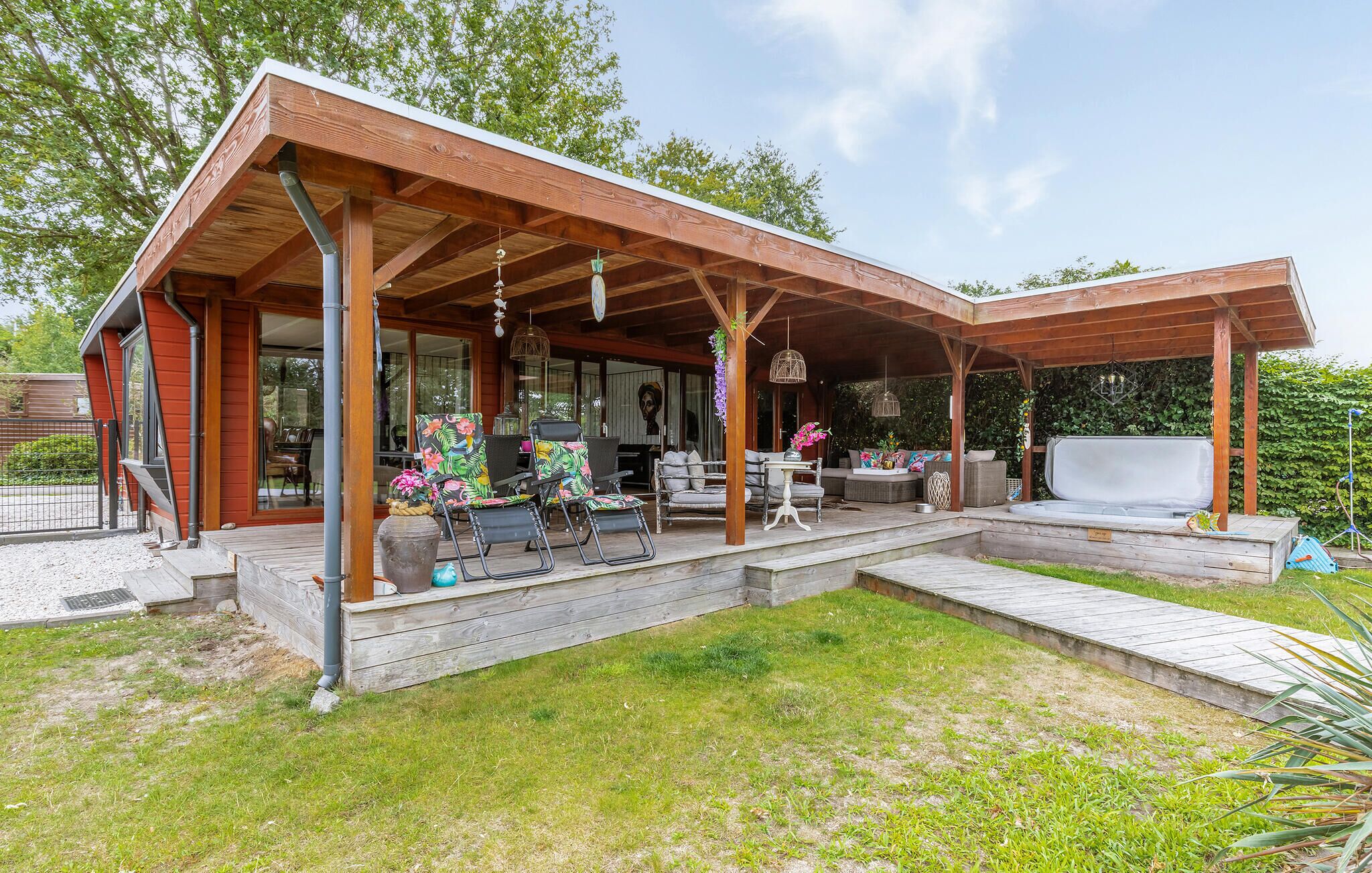 A covered outdoor patio with seating and a table, surrounded by a wooden deck and a grassy area.