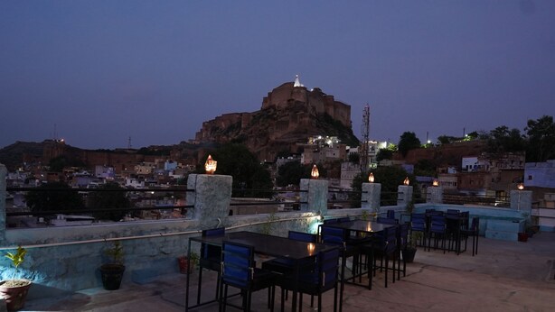 Terraza en la azotea con mesas y sillas, con vista a una fortaleza histórica y edificios circundantes.