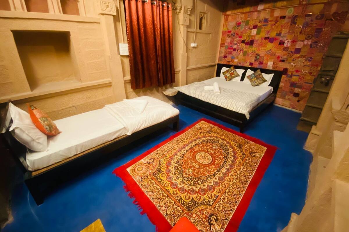 A room with two beds, a red patterned rug, and a colorful quilt on the wall.