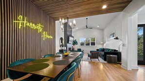 Un espace repas moderne avec une table en bois et des chaises de couleur turquoise, un néon et une cuisine en arrière-plan.