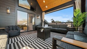 Un espace de vie extérieur moderne avec un sol à carreaux, un canapé noir, un fauteuil poire et une table.