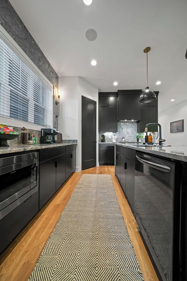 A modern kitchen with dark cabinetry, a patterned rug, and a window with blinds.