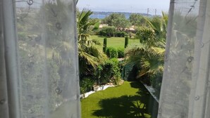 A view through a window with a patterned curtain, revealing a well-maintained garden with various plants and a clear sky. - Magnificent sea view (Juan les Pins)